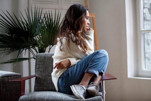 Lonely and worried girl sitting alone on a chair looking out a window.