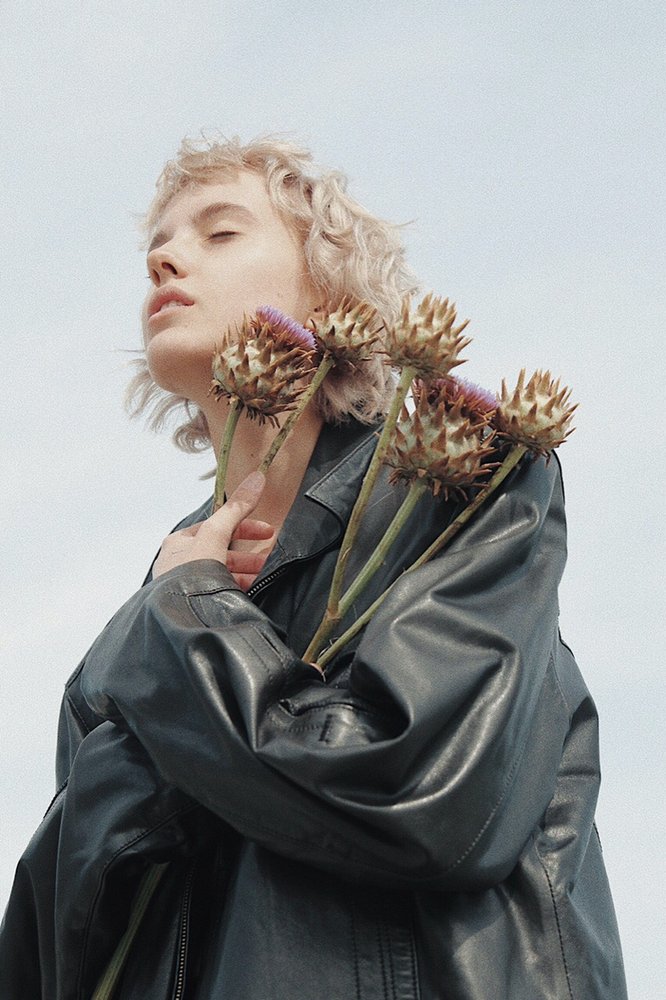 blonde hair woman in leather jacked holding flowers